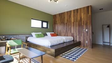 A modern bedroom with a wooden platform bed, a green chair, a small table, and a window.