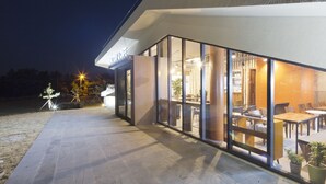 Un edificio moderno con grandes ventanales, un patio con mesas al aire libre y un interior bien iluminado.