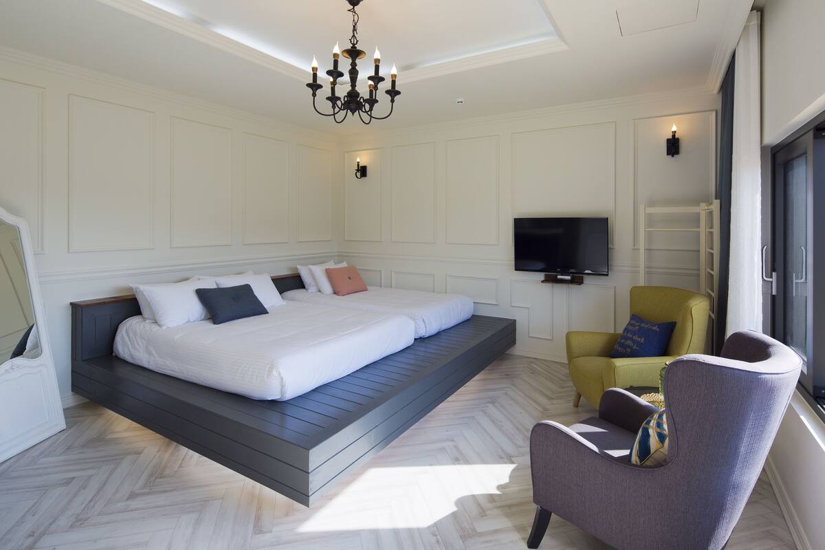 A bedroom with a bed, a chair, a TV, and a chandelier.