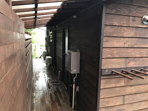 A wooden building with a covered porch, a utility box, and a metal handle on the wall. - Preta Torami - Hostel (Ichinomiya)