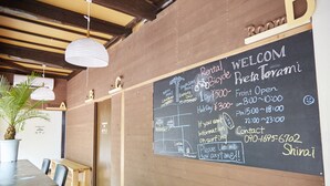 A room with a chalkboard displaying a welcome message, room names, and a contact number. - Preta Torami - Hostel (Ichinomiya)
