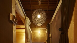 A narrow wooden hallway with a hanging light fixture, wooden benches, and curtains. - Preta Torami - Hostel (Ichinomiya)