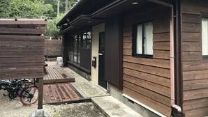 A wooden cabin with a porch, a bicycle, and a small outdoor seating area. - Preta Torami - Hostel (Ichinomiya)