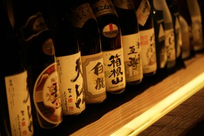 A row of bottles with labels, likely containing beverages, arranged on a wooden surface. - Masutomi Ryokan (Hakone)
