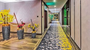 A hotel hallway with a patterned carpet, potted plants, and a green wall. - Guangzhou Kardon Hotel Gorgeous (Guangzhou)
