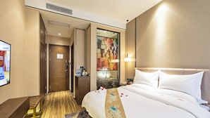 A hotel room with a bed, a desk, a chair, a small table with a lamp, and a wall-mounted TV. - Guangzhou Kardon Hotel Gorgeous (Guangzhou)