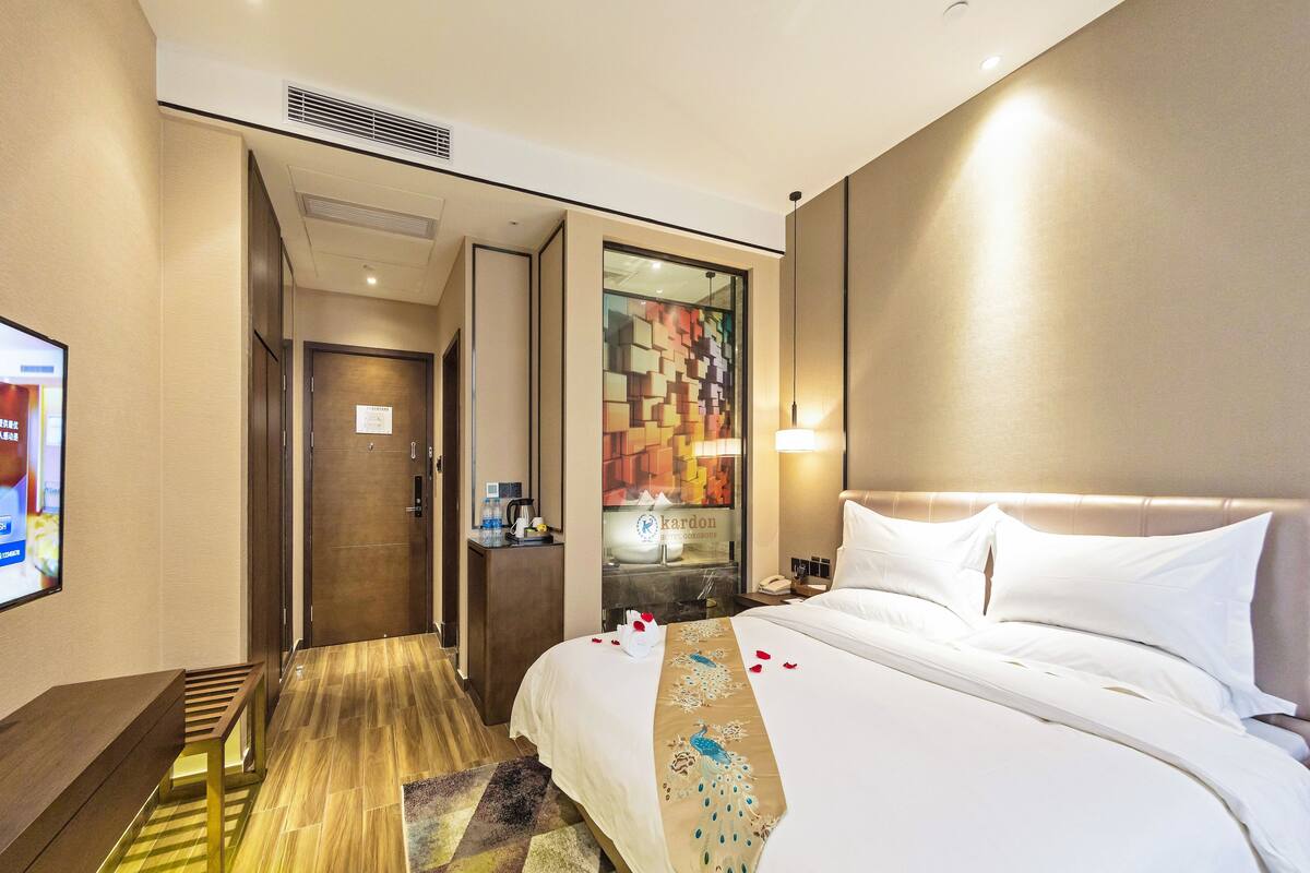 Een hotelkamer met een bed, een bureau, een stoel, een klein tafeltje met een lamp en een tv aan de muur.