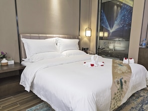 A hotel room with a large bed, white linens, a nightstand with a vase of flowers, and a window with a cityscape view.
