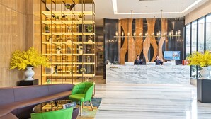 A modern hotel lobby with a reception desk, seating area, and a decorative plant display. - Guangzhou Kardon Hotel Gorgeous (Guangzhou)