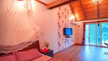 A bedroom with a bed, a TV, a nightstand, a window, and a wooden ceiling.