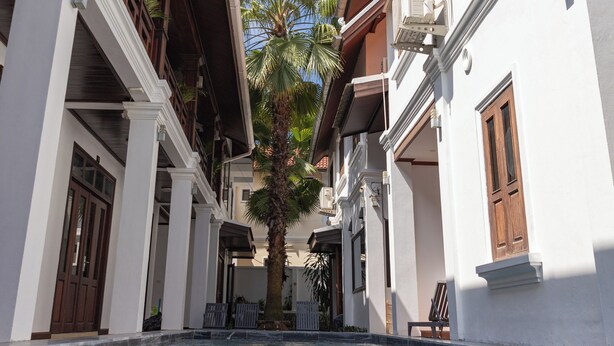 A swimming pool with a clear view of the sky, surrounded by white buildings with wooden balconies and palm trees.