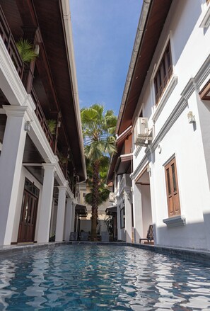 Una piscina con una vista despejada del cielo, rodeada de edificios blancos con balcones de madera y palmeras.