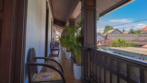A covered balcony with wooden railings, potted plants, and a chair with a floral cushion.