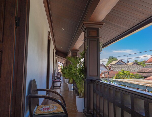 Un balcone coperto con ringhiere in legno, vasi con piante e una sedia con cuscino fiorito.