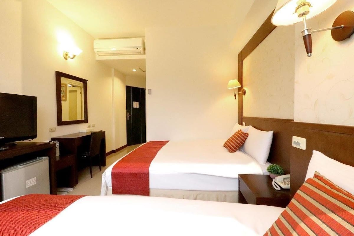 A hotel room with two beds, a desk with a television, and a mirror.