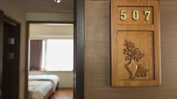 Un panneau mural en bois portant le numéro 507, un vase sculpté orné de fleurs et une petite table sur laquelle sont disposés des fruits.