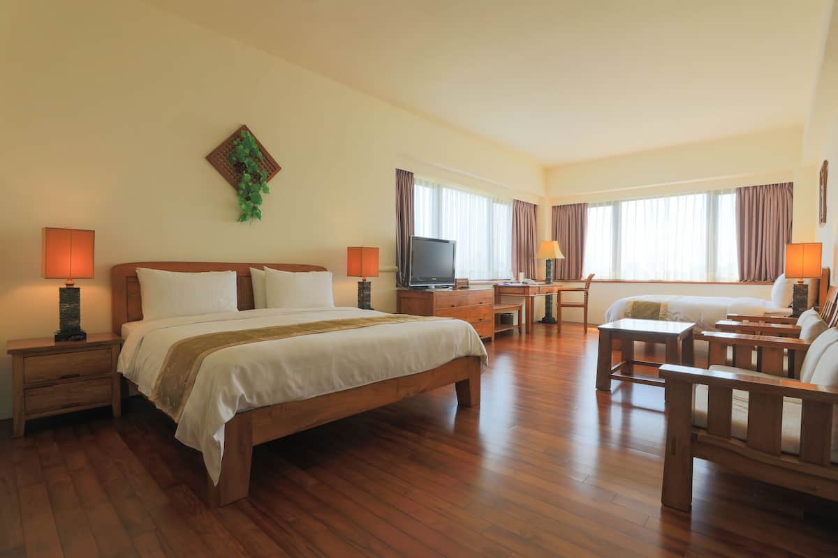A hotel room with a large bed, a desk, a TV, and a seating area with chairs.