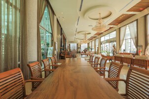 Un comedor amplio con una larga mesa de madera y múltiples sillas de madera, ventanas grandes y candelabros.