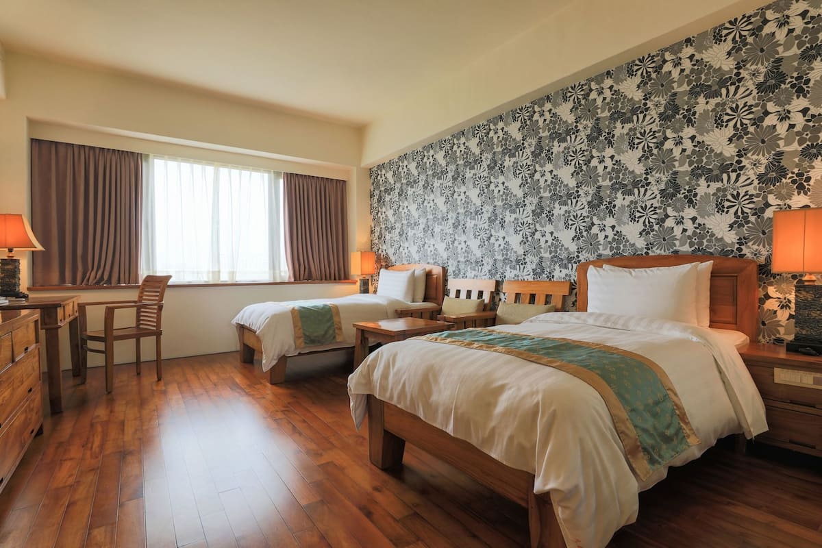 A hotel room with two beds, a desk, a chair, and a window with curtains.