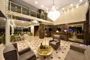 Eine geräumige Lobby mit hoher Decke, einem Chandelier und einem Schachbrettmuster-Boden. Es gibt mehrere Sitzbereiche und eine Rezeption.