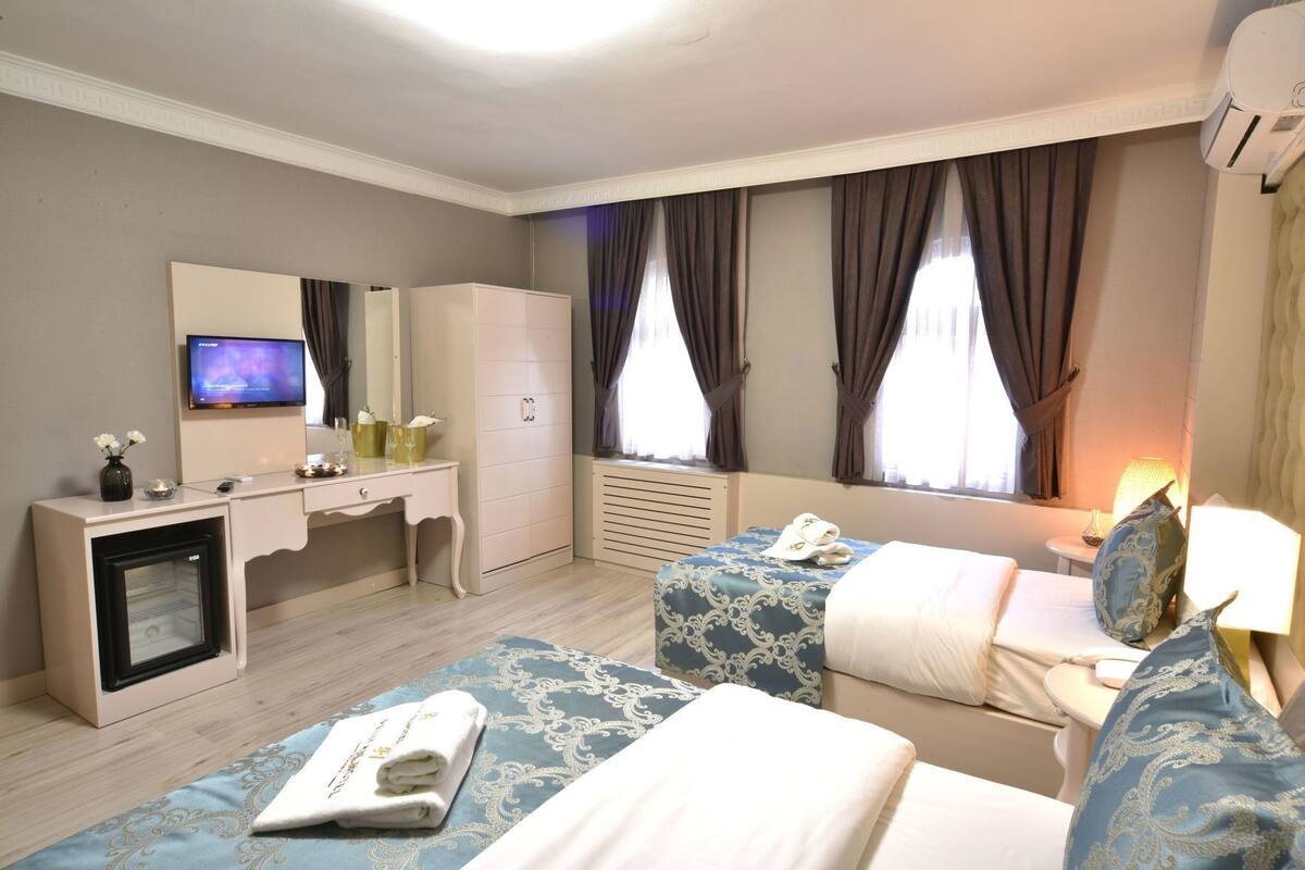 A hotel room with a bed, a desk, a television, a wardrobe, and a window with curtains.