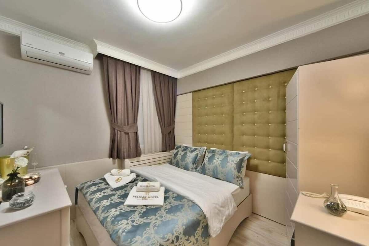A hotel room with a bed, a wardrobe, a bedside table with a lamp, and an air conditioning unit.
