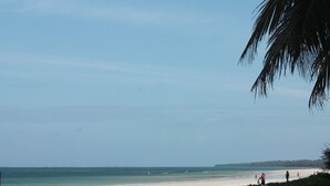 A beach with clear skies, calm waters, and a few people walking along the shore. - Galu Tulivu (Diani Beach)