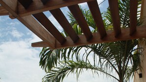 A swimming pool with a pergola overhead, surrounded by lush greenery and a stone wall. - Galu Tulivu (Diani Beach)