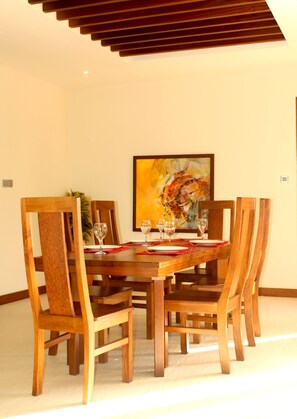 A dining area with a wooden table and chairs, a painting on the wall, and a ceiling with wooden slats.