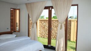 A bedroom with a bed, curtains, and a view of a stone wall and greenery outside. - Galu Tulivu (Diani Beach)
