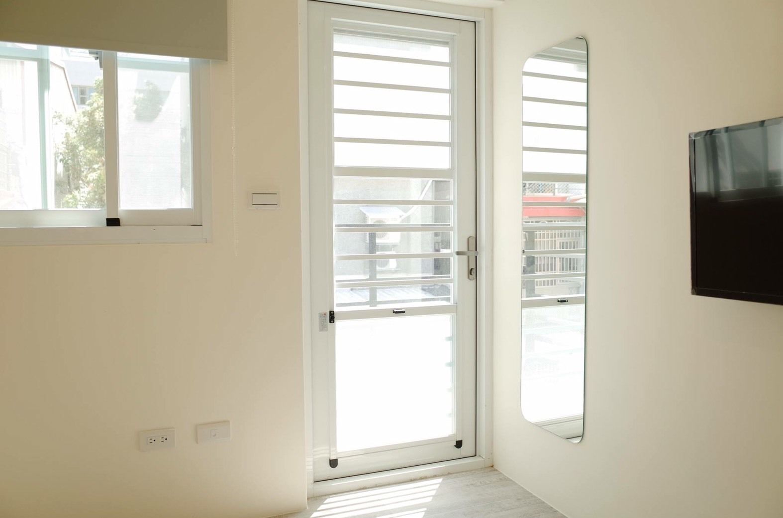 Ein Zimmer mit einer Schiebeglasdoor zum Balkon, einem Wandfernseher und einem Fenster mit Jalousien.