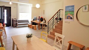 A spacious room with a wooden table and chairs, a staircase, and a wall with a poster. - Chestnut Guest House (Taitung)