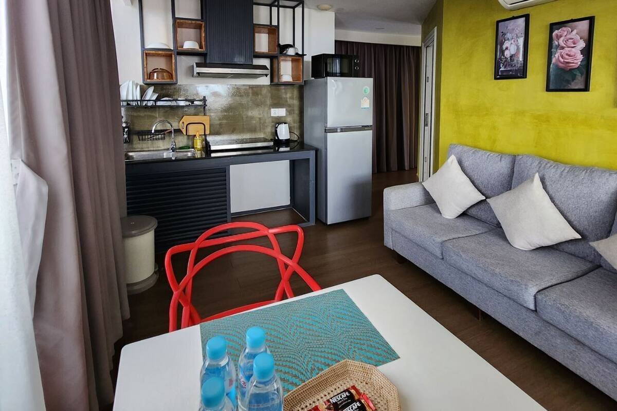 A compact living space with a kitchenette, a grey sofa, and a red chair.