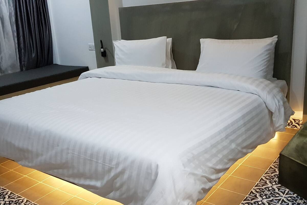 A neatly made bed with white linens, a headboard, and a bedside lamp.