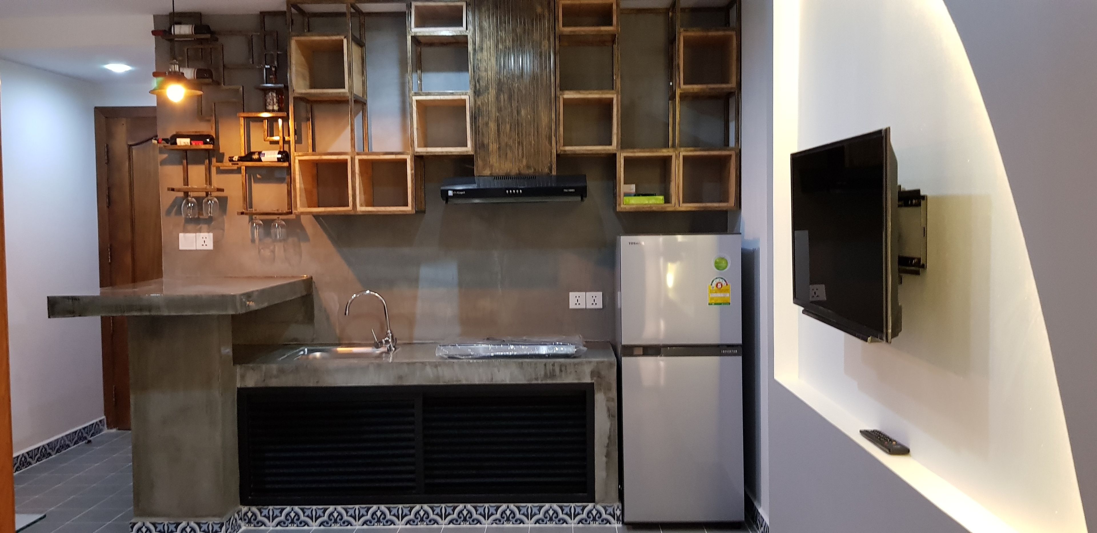 Eine moderne Küche mit eingebauten Holzböden, einem Edelstahlkühlschrank und einem an der Wand befestigten Fernseher.