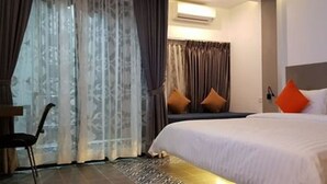 A hotel room with a large bed, a desk, and a chair. There is a window with curtains and an air conditioning unit above it. - Katy Resident and Spa (Siem Reap)