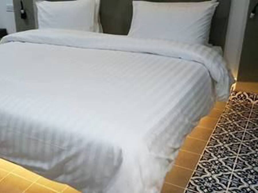 Ein ordentlich bezogenes Bett mit weißen Leinentüchern in einem Raum mit gemusterten Fliesen.