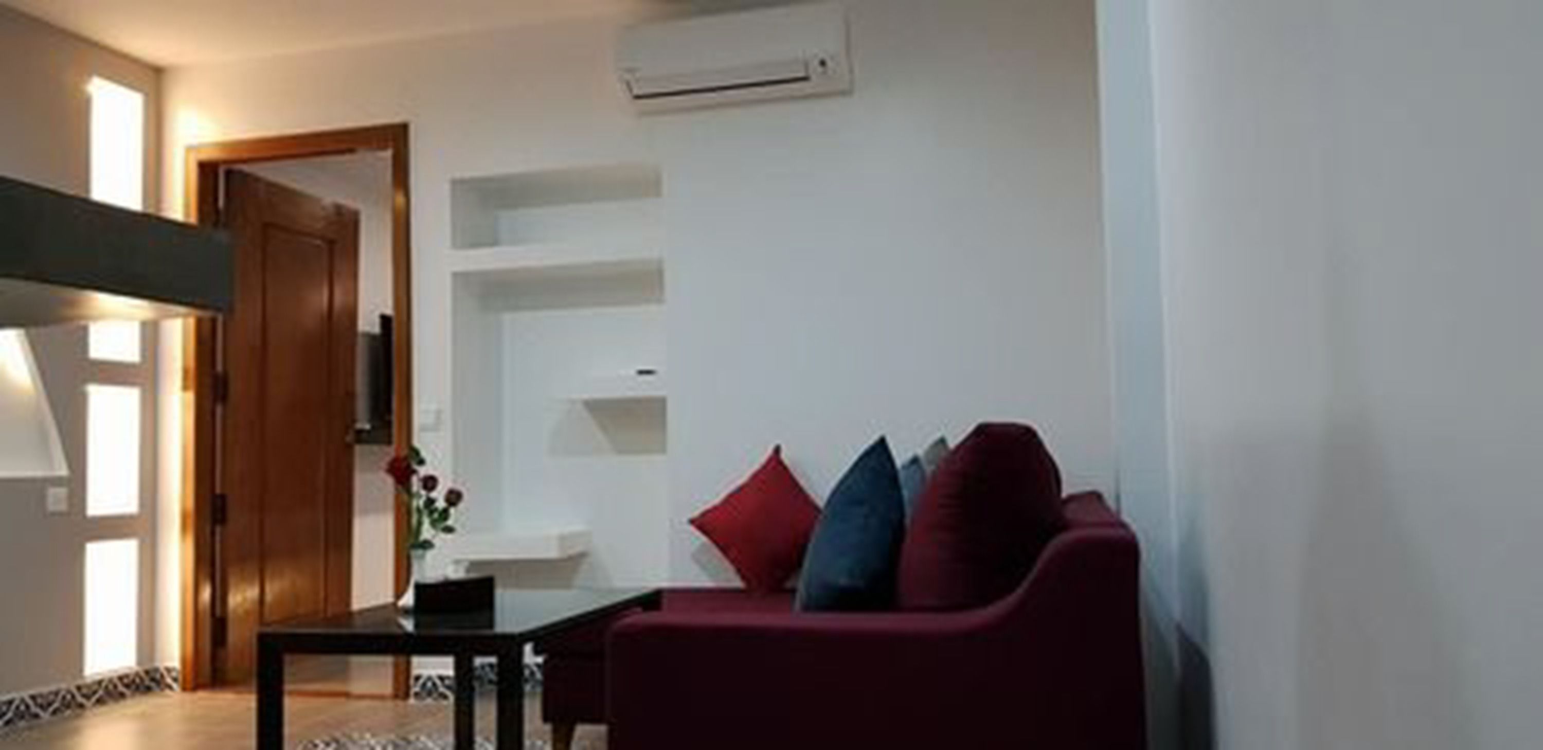 A living room with a red sofa, a small table, and a white wall with built-in shelves.