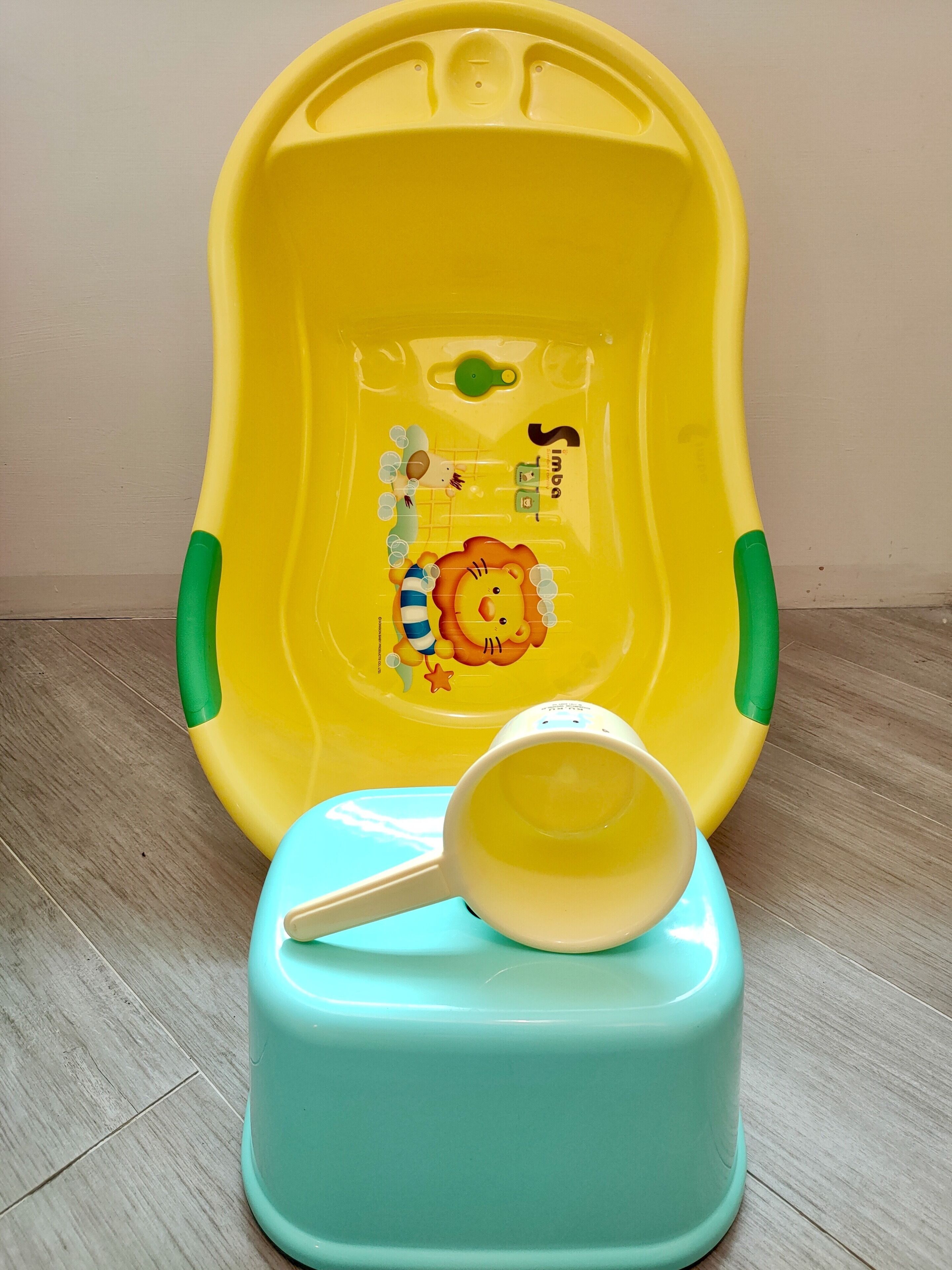 Een gele en groene plastic bak met een leeuw erop, op een houten vloer geplaatst.