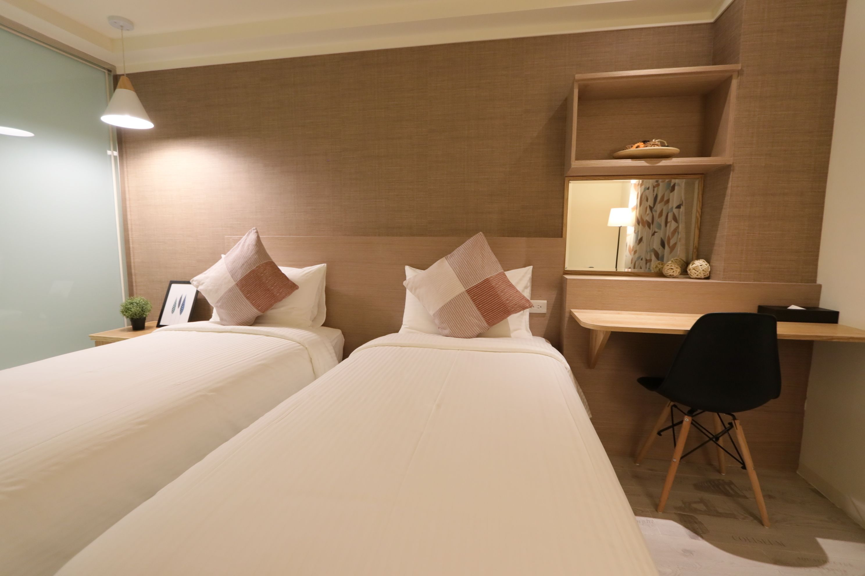 Habitación de hotel con dos camas, un escritorio, una silla y un estante con objetos decorativos.