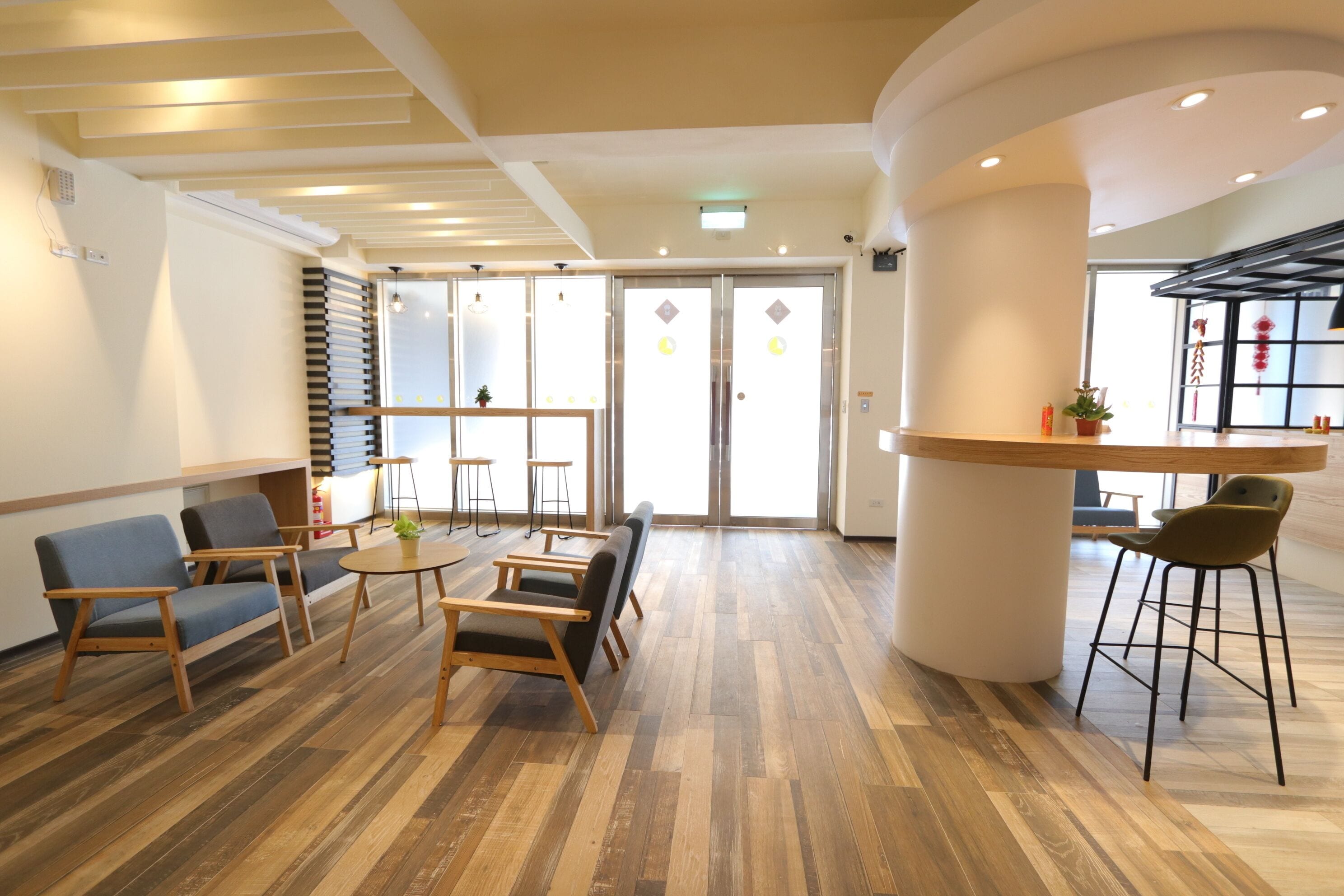 A modern interior with wooden flooring, a central seating area with chairs and a table, and a bar counter.