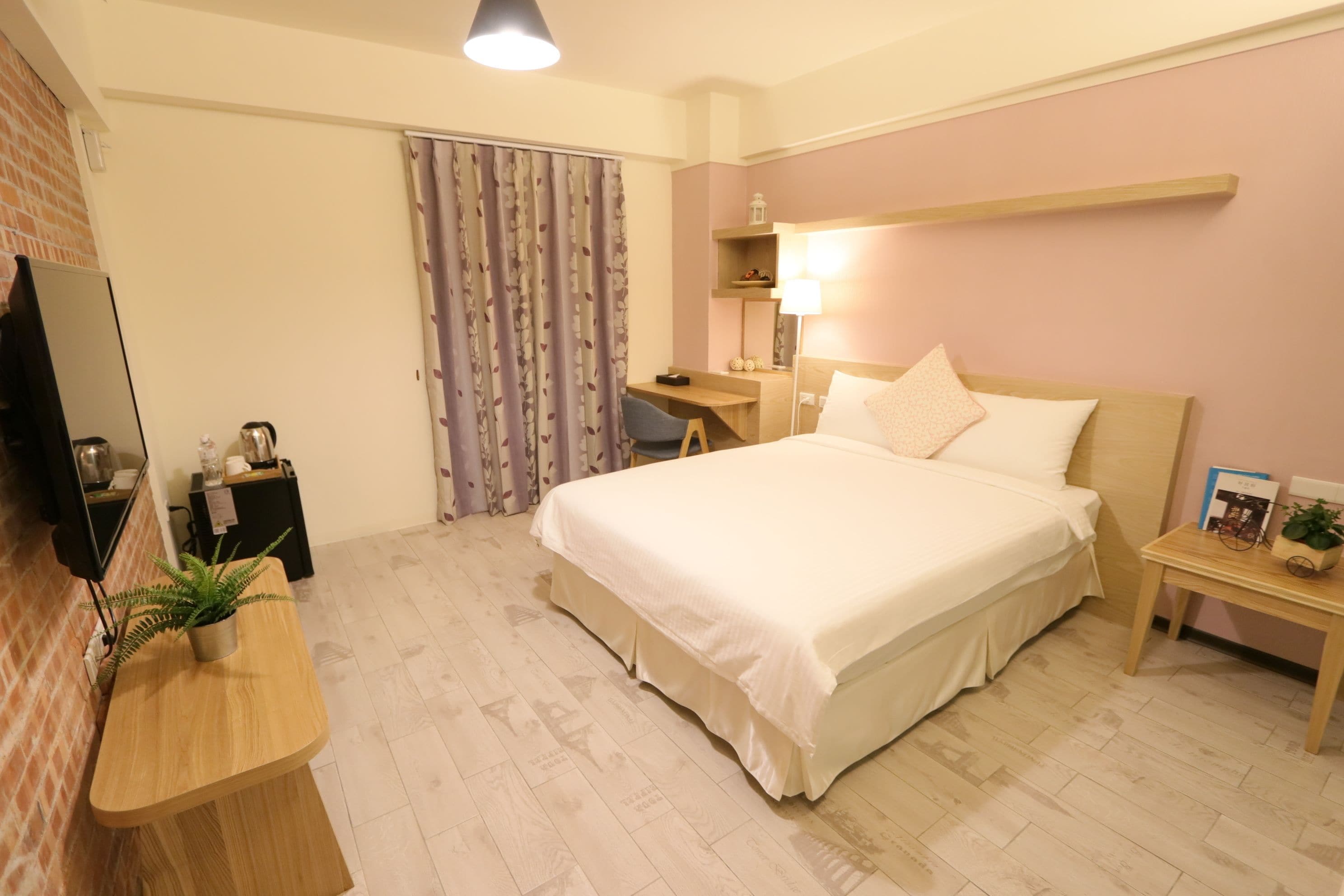 A hotel room with a bed, a desk, a chair, a TV, and a plant.