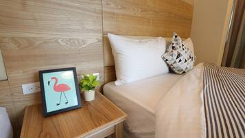 Habitación de hotel con cabecera de madera, cama con ropa de cama blanca, mesita de noche con un cuadro enmarcado de un flamenco y una pequeña planta en maceta.
