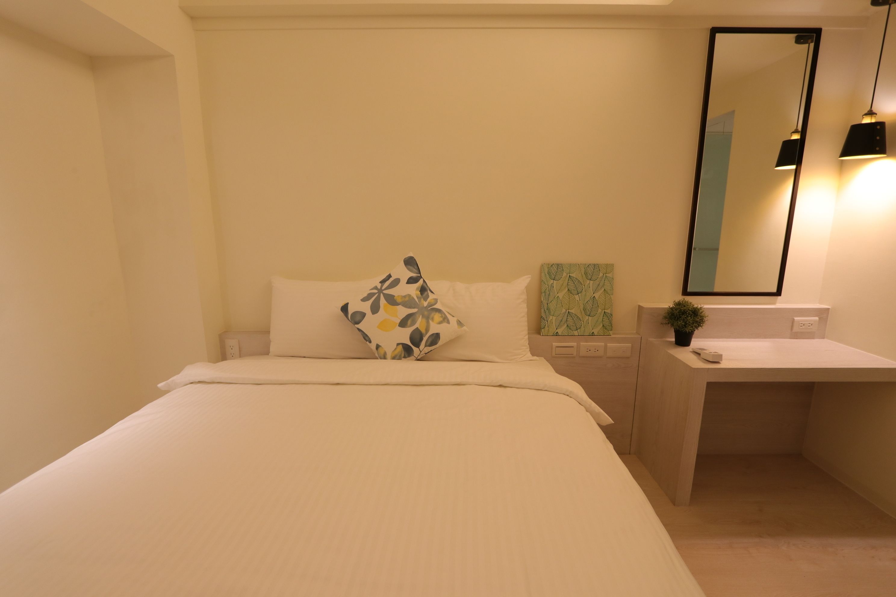 A bedroom with a bed, a bedside table, a mirror, and a small potted plant.
