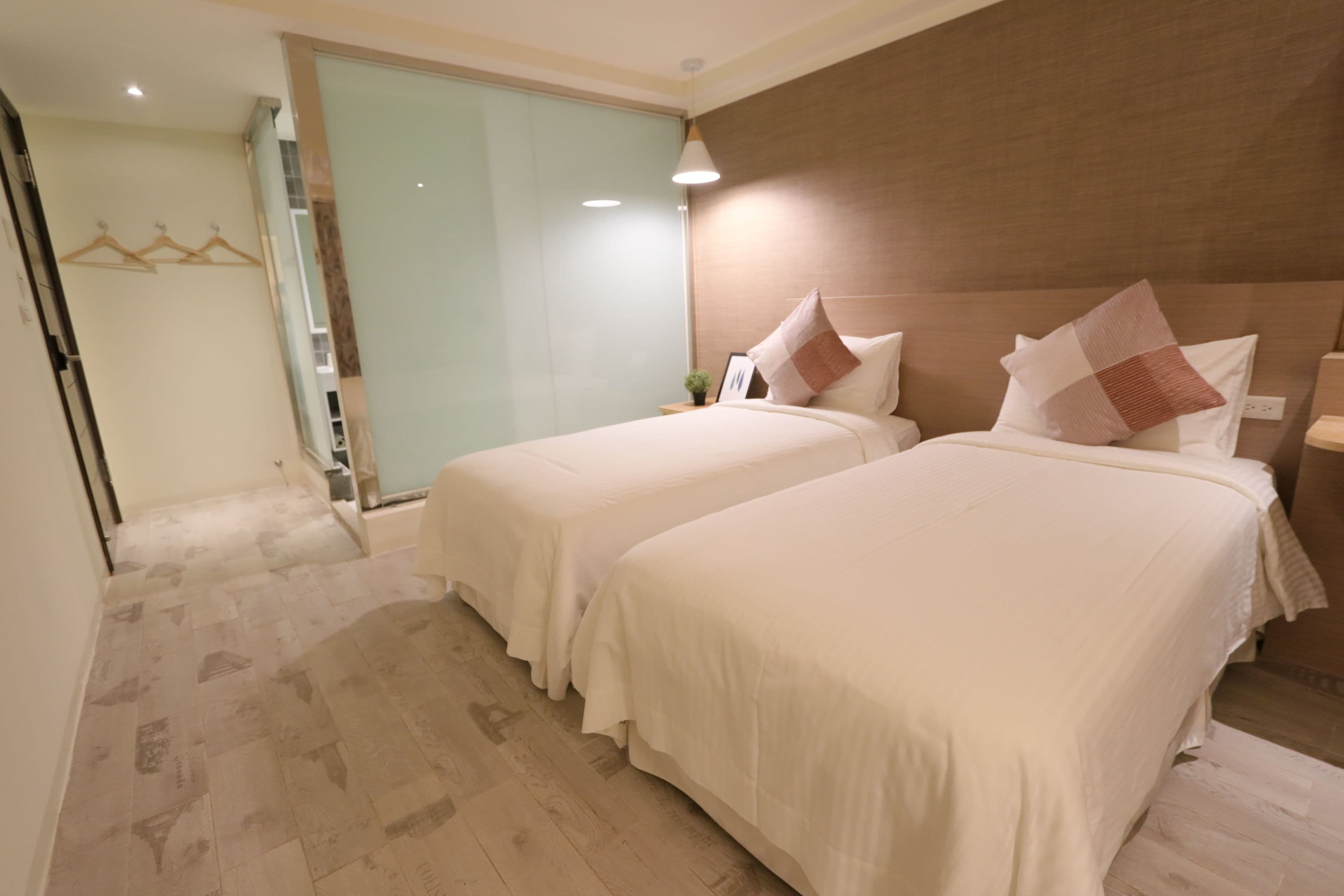 Une chambre d’hôtel avec deux lits, un plancher en bois, une porte en verre et une lampe fixée au mur.