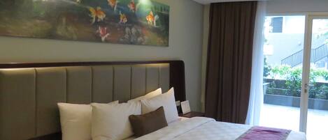 A hotel room with a large bed, a headboard, a painting of fish, and a view of a building through a window.