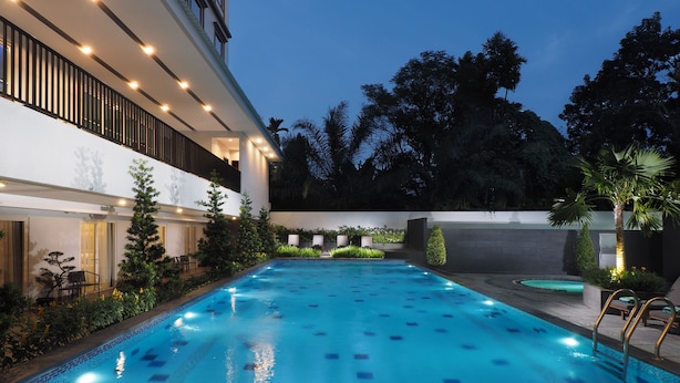 A swimming pool with a modern design, surrounded by a landscaped garden and a building with a balcony. - d'primahotel Kualanamu Medan (Medan)