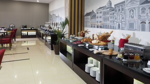 A hotel breakfast area with a buffet, dining tables, chairs, and a mural of buildings on the wall. - d'primahotel Kualanamu Medan (Medan)