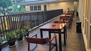 A covered outdoor seating area with tables and chairs, potted plants, and a view of the sky and buildings. - d'primahotel Kualanamu Medan (Medan)