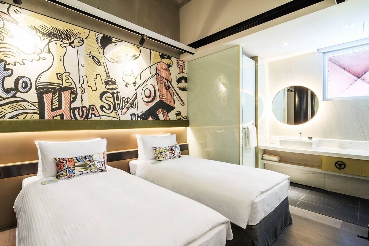 A hotel room with two beds, a large mural on the wall, a modern bathroom with a round mirror, and a minimalist design.
